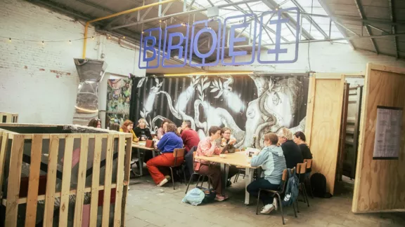 jongeren die aan tafeltjes zitten met het logo van BROEI erboven